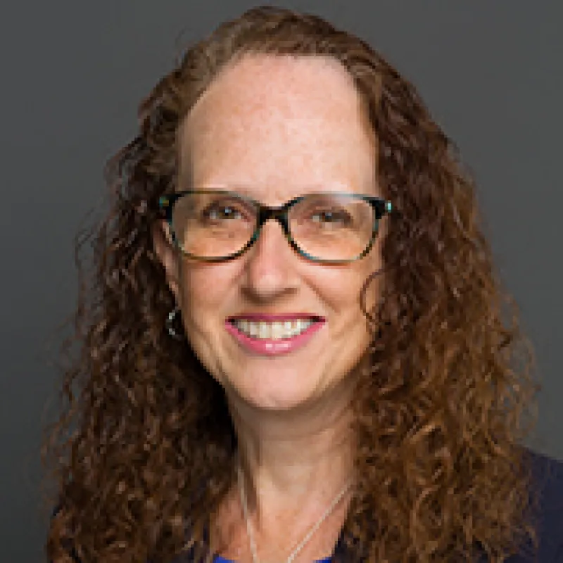 Professional headshot of a woman with curly brown hair who is wearing glasses.