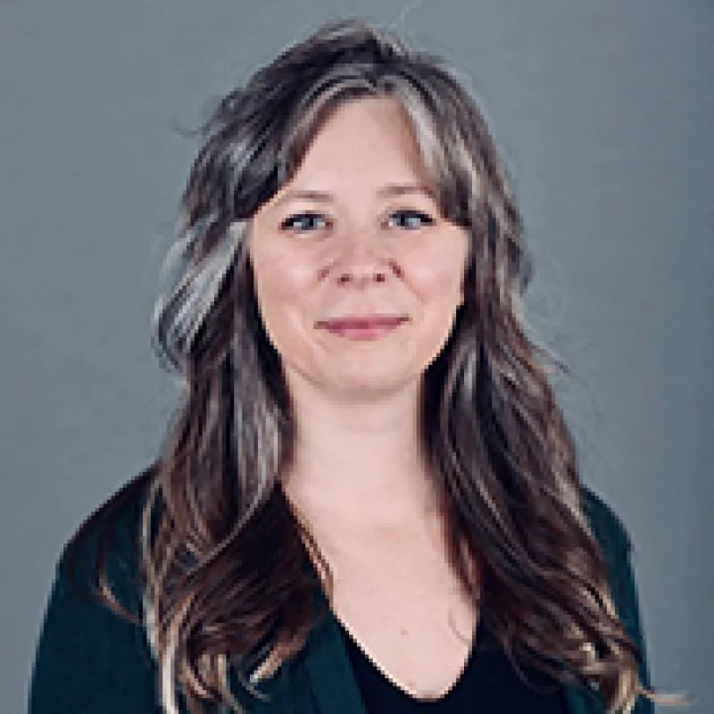 Professional headshot of woman with long hair who is wearing a dark-colored shirt.