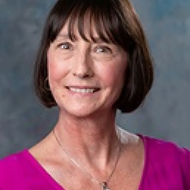 Professional headshot of a woman with short, dark brown hair who is wearing a pink shirt.