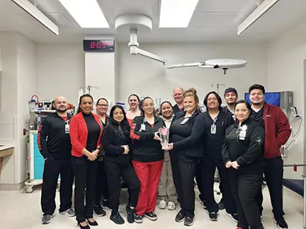 Group photo of the Uvalde ED team in a hospital setting, dressed in black and red uniforms, smiling and posing together while holding a recognition award.