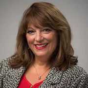 Professional headshot of a woman with brown hair who is wearing a striped suit coat and a red shirt.