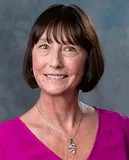 Professional headshot of a woman with short, dark brown hair who is wearing a pink shirt.