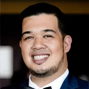 Photo of a man with short dark hair smiling who is wearing a suit.