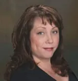 Headshot of a woman with shoulder-length brown hair, wearing a black top, looking confidently at the camera with a slight smile.