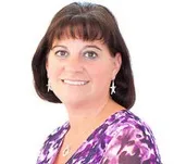 A professionally taken headshot of a woman with straight, dark brown hair, wearing a vibrant purple patterned blouse.