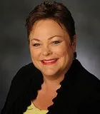 Headshot of a woman with short brown hair, wearing a black blazer and a yellow top, smiling warmly.