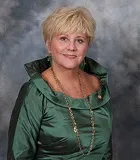 A professional portrait of a woman with short blonde hair wearing an elegant green dress with a high collar. She accessorizes with long gold earrings and a matching necklace.A professional portrait of a woman with short blonde hair wearing an elegant green dress with a high collar. She accessorizes with long gold earrings and a matching necklace.