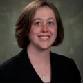 A portrait of a woman with short, straight brown hair and light skin. She is smiling and wearing a black blazer over a light top.