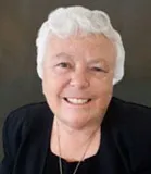 Headshot of a woman with short white hair, wearing a black blazer and a necklace, smiling warmly.