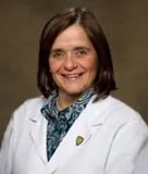 Headshot of a woman with shoulder-length brown hair, wearing a white coat over a patterned blouse, smiling warmly