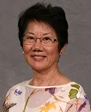 Headshot of a woman with short black hair, wearing glasses and a white floral-patterned top, smiling warmly.