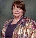 Headshot of a woman with short brown hair, wearing a multicolored patterned jacket over a purple top, smiling subtly.