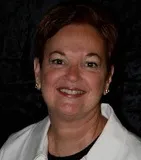 A portrait of a woman with short auburn hair and light skin. She is smiling warmly and wearing a white blouse and small gold earrings.